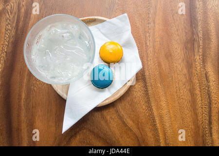Welcome drink set with fresh ice-water, blue and orange colors magaroons and white nepkin in wooden tray on wooden table. Stock Photo
