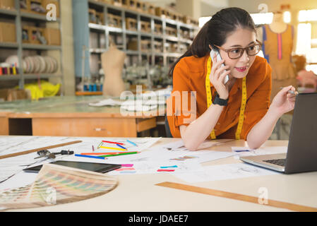 Multiethnic Asian girl leaning on the table and discuss on the phone in manufacturing office studio. profession and job occupation concept. Stock Photo