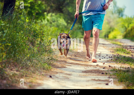 A man runs barefoot with a dog on a dirt road in summer Stock Photo