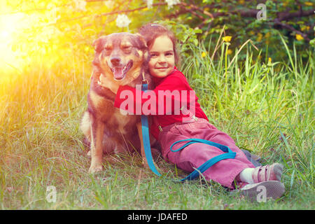 Little girl and dog are best friends. Girl sitting on the grass and hugs the dog Stock Photo