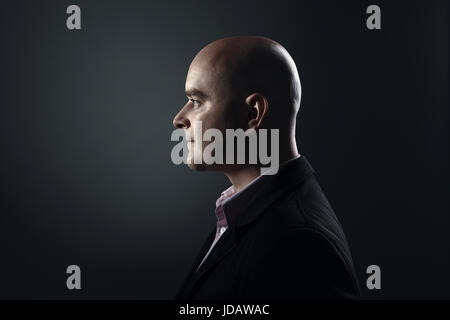 Profile of white bald man in his twenties in dark Stock Photo