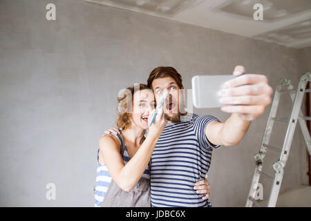 Couple at home painting walls, taking selfie with smartphone. Stock Photo