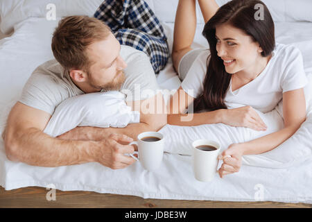 Couple maintaining eye contact while relaxing in bed with coffee Stock Photo