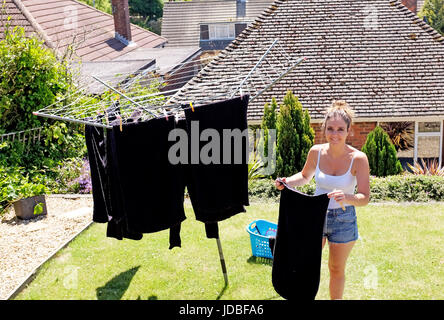 Young woman in her 20s hanging out washing to dry in back garden on a hot summers day UK Stock Photo