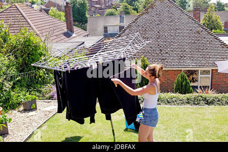 Young woman in her 20s hanging out washing to dry in back garden on a hot summers day UK Stock Photo