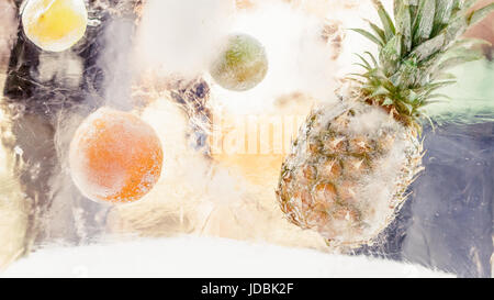 Block of ice with frozen tropical fruits, pineaple, orange, lime, lemon. Summer refreshment concept Stock Photo