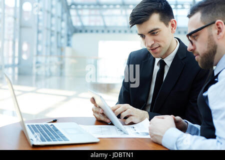 Portrait of two business partners using digital tablet and laptop in meeting, discussing deals Stock Photo