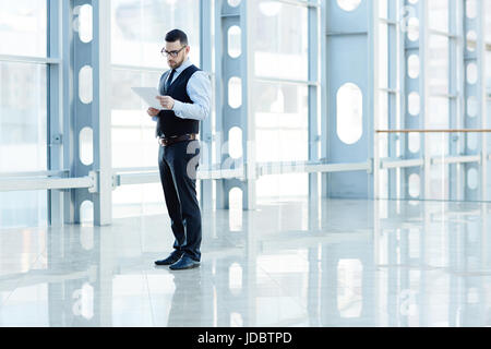 Portrait of contemporary successful businessman reading documents in hall of modern office building, copy space Stock Photo