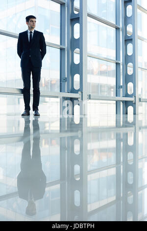 Wide angle portrait of modern business expert standing confidently in hall of futuristic glass office building Stock Photo