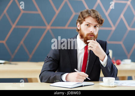 Businessman thinking of ideas and writing them down in notebook Stock Photo
