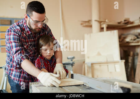 Young man and boy processing wooden workpiece on planing machine Stock Photo