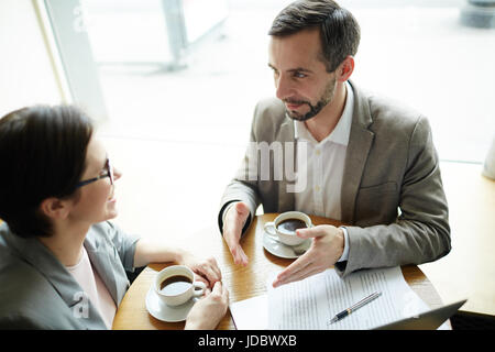 High angle portrait of two enthusiastic adult business people discussing project during coffee break in cafe Stock Photo