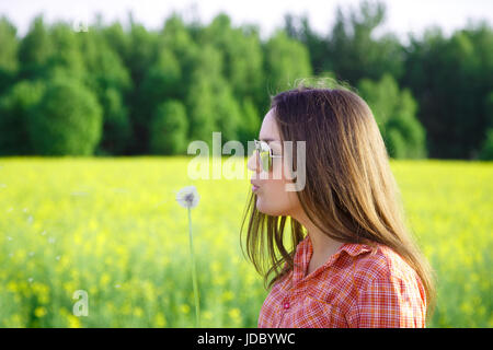 Young woman with sunglasses blowing on a dandelion in the summer Stock Photo