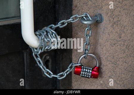 Red code lock hanging on the chain, closing the front door. Stock Photo