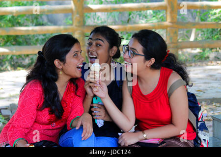 Three beautiful young indian women enjoying and sharing a single cone of ice cream in summer vacation and showing love and true friendship. Stock Photo