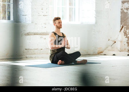 Young candid man sitting on a fitness mat and meditating in the gym Stock Photo