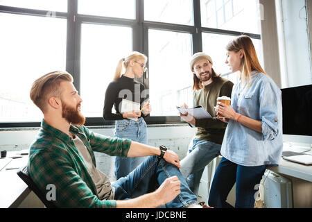 Image of young colleagues standing in office and talking with each other. Looking aside. Stock Photo
