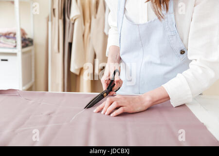 Cropped image of woman seamstress using scissors to cut fabric in workshop Stock Photo