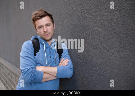 Caucasian handsome man in casual clothes with a friendly smile leaning against wall with a rough texture outdoors Stock Photo