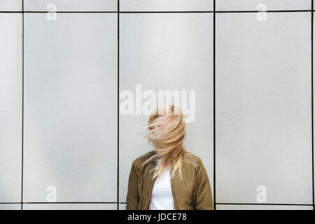 Funny blonde woman shaking her hair against grey wall Stock Photo