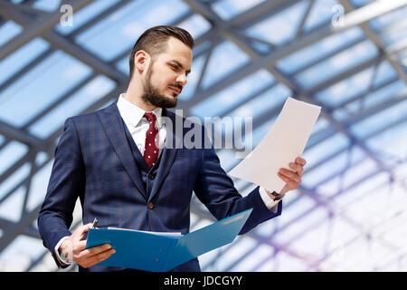 Portrait of mature businessman holding binder and documents over modern building interior background Stock Photo
