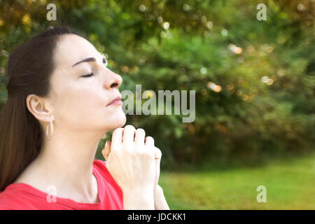 Portrait of a woman outdoors, closed eyes and hands together, wishing, praying. Stock Photo
