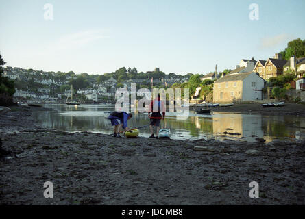 two male canoeists setting off at Evening sunset at Noss Mayo in the estuary at low tide, Devon, England, UK Stock Photo