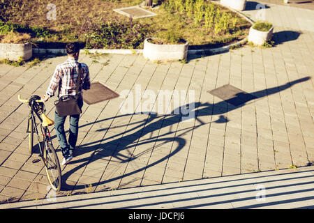 Rear view of a casual businessman going to work by bicycle. He is pushing bike. Stock Photo