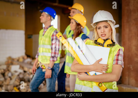 Beautiful young female construction architects at a construction site. She is holding plans and looking at camera. Stock Photo