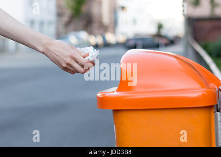 Throwing waste into a an orange trash can in the street from the side Stock Photo