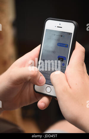 Close Up of Teenage boy aged 19 years using an Apple iPhone SE mobile phone to read and send text messages Stock Photo