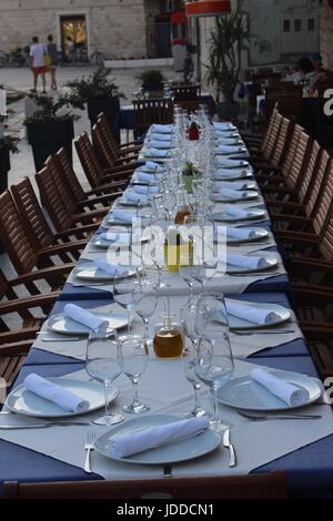 Long Table laid with white cloth, glasses and cutlery for twenty four people outside in sunshine Stock Photo