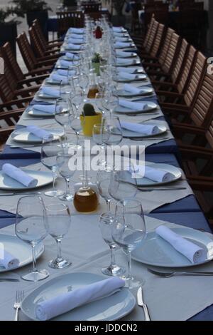 Long Table laid with white cloth, glasses and cutlery for twenty four people outside in sunshine Stock Photo