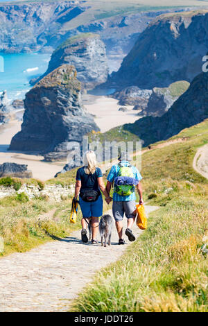 A man and woman couple walking down the path towards the beach at the popular attraction of Bedruthan Steps in Cornwall on a hot summers day holding hands in love Stock Photo