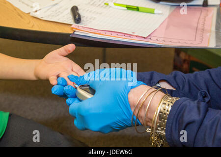 A staff worker at an elementary school checks the blood sugar level of a six-year-old boy with type 1 diabetes, also called juvenile diabetes. His blo Stock Photo