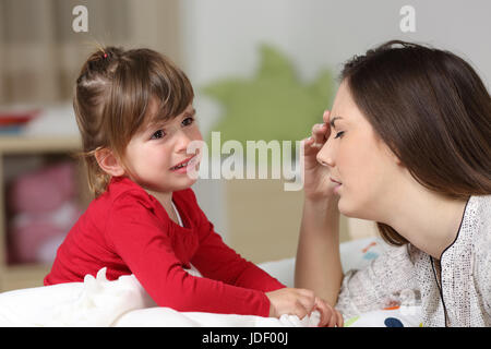Fed up woman listening to her two years old daughter crying sitting on the bed in a house interior Stock Photo