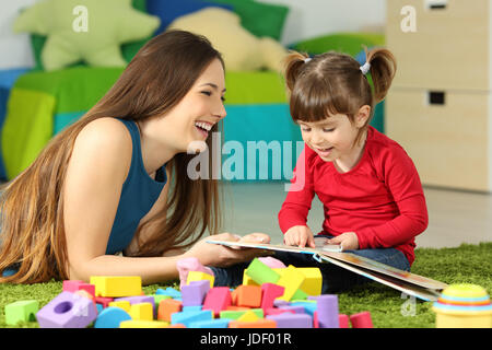 Mother and toddler playing together with a book lying on the floor in the bedroom at home with a colorful background Stock Photo