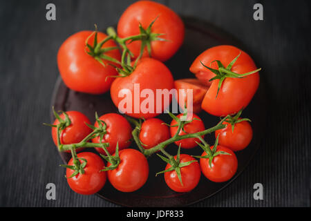 Fresh red ripe tomatoes with water drops on branches on black background. Close-up. Selective focus. Top view. Low key. Concept of vegetarian, healthy food. Stock Photo