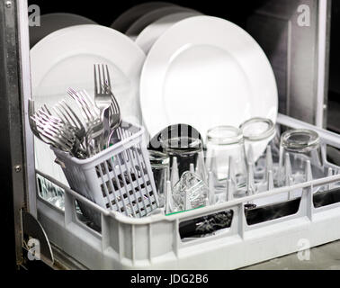 Clean generic white dishes, glasses and cutlery in a dishwasher viewed close up through the open door Stock Photo