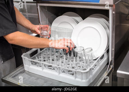 Male hand removing clean washed generic white dishes and glasses from an open dishwasher in a close up view Stock Photo