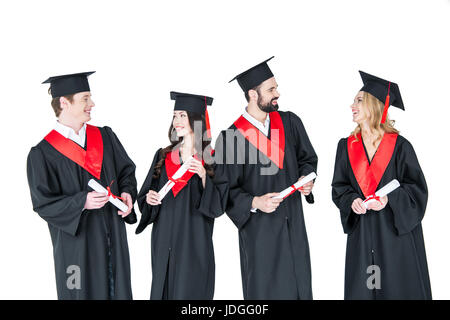 Group of young men and women in graduation gowns and mortarboards holding diplomas Stock Photo