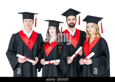 Group of young men and women in graduation gowns and mortarboards holding diplomas Stock Photo