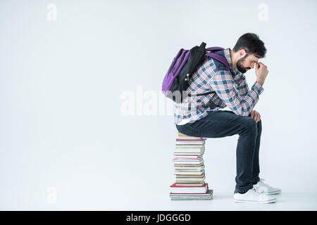 tired bearded student sitting on pile of books on white with copy space Stock Photo