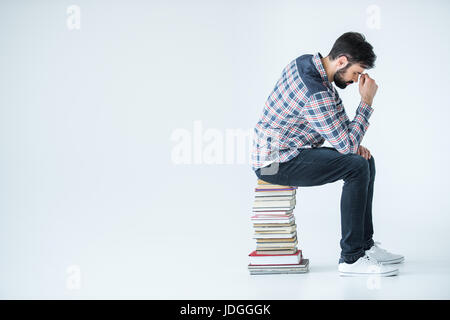 tired bearded student sitting on pile of books on white with copy space Stock Photo