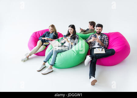 students sitting on beanbag chairs and studying and using smartphones in studio on white Stock Photo