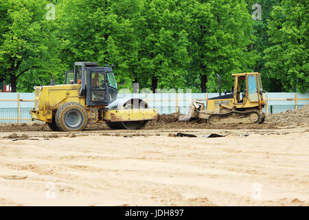 tractor and compactor are leveling and compacting the surface of the earth. Construction of the city stadium Stock Photo