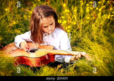 Child Sitting in the Tall Grass Playing Guitar Stock Photo