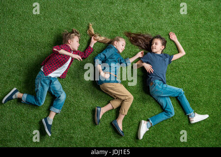 Top view of three adorable children lying together on green lawn Stock Photo