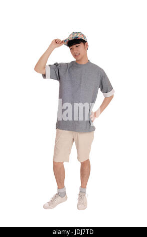 A young Asian teenager standing in shorts an a gray t-shirt with his hand on his cap, isolated for white background. Stock Photo