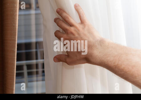 Hand opens soft white tulle on window, first person view Stock Photo